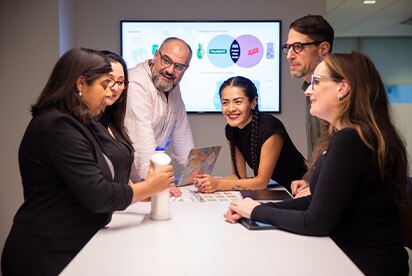 Seis empleados de Colgate-Palmolive en una sala de reuniones analizando un concepto de producto, con una diapositiva de presentación en una pantalla detrás de ellos.